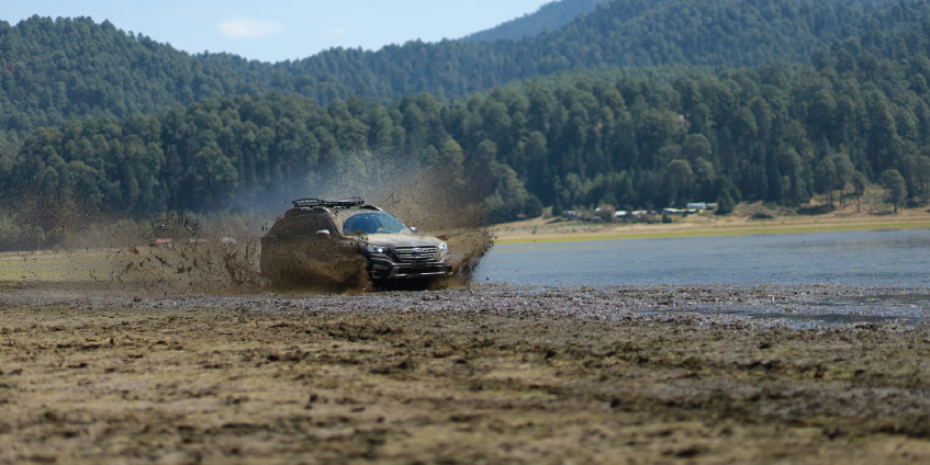 Camioneta 4x4 Subaru sobre terreno de lodo y laguna con vegetación de fondo.